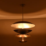 Night-view of a tiered metal disc pendant light displaying soft glowing reflections across layered metallic bowls.