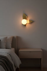 Brass leaves glass globe wall sconce shown from front with artistic folded brass panels and soft warm light