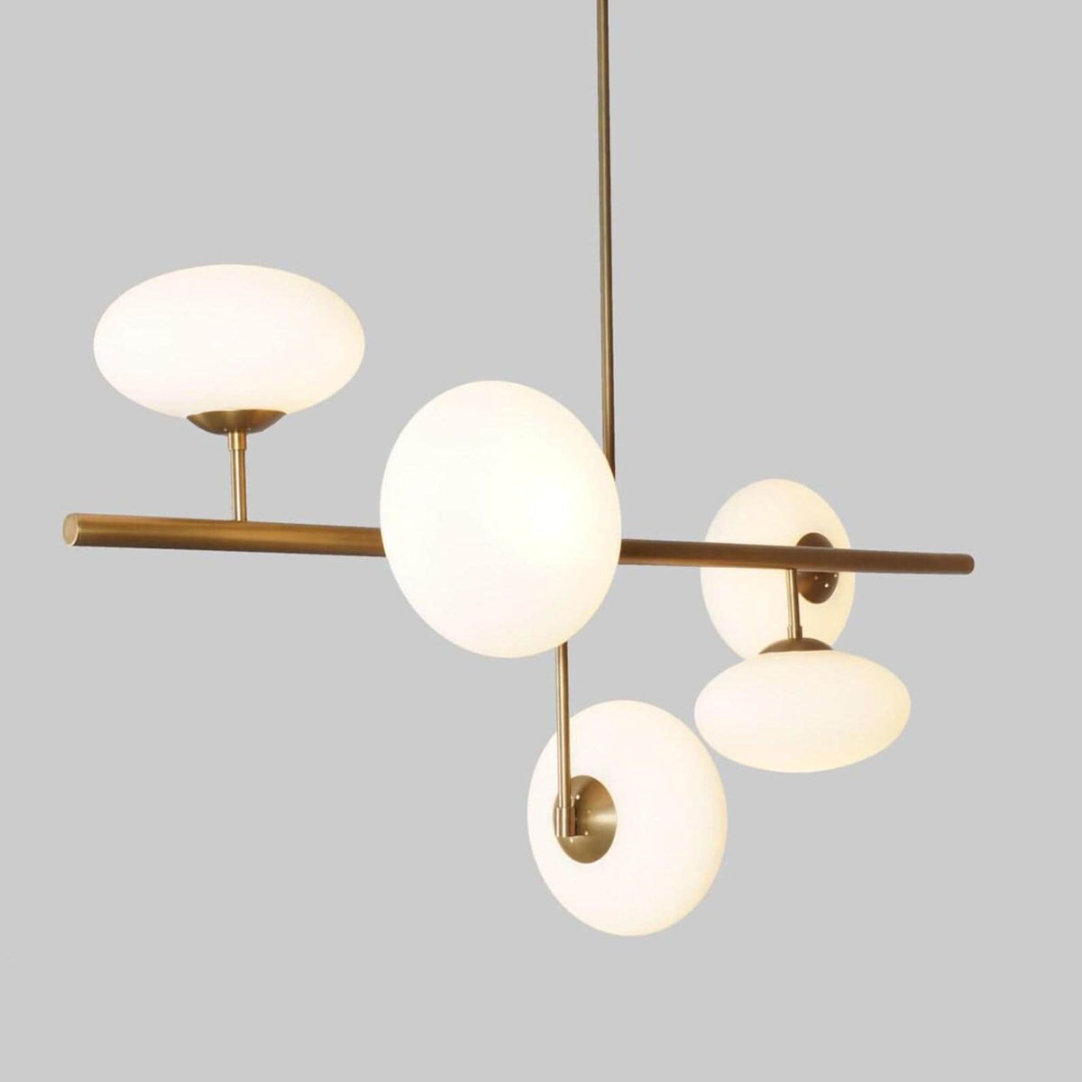 Side view of a handcrafted brass linear chandelier with five milky glass globes, showcasing balanced proportions and minimalist industrial style.