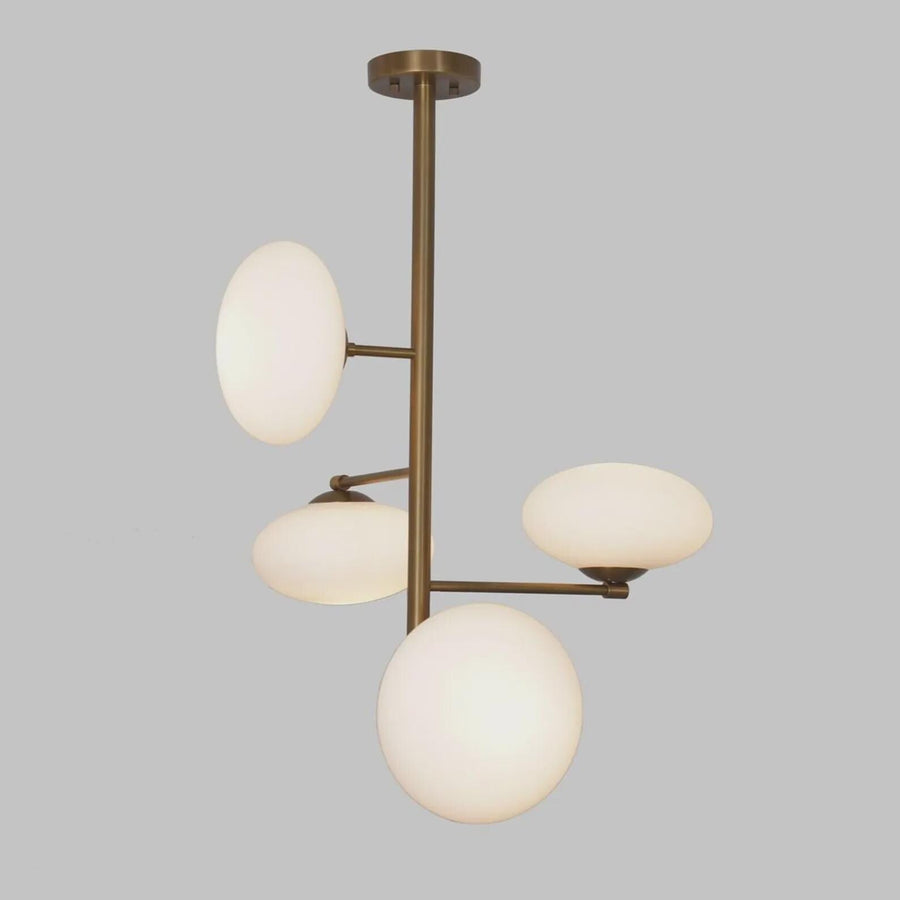 Modern 4-light brass chandelier with milky glass globe shades, featuring a vertical sculptural design and warm ambient lighting by Brass Leaf Studio.