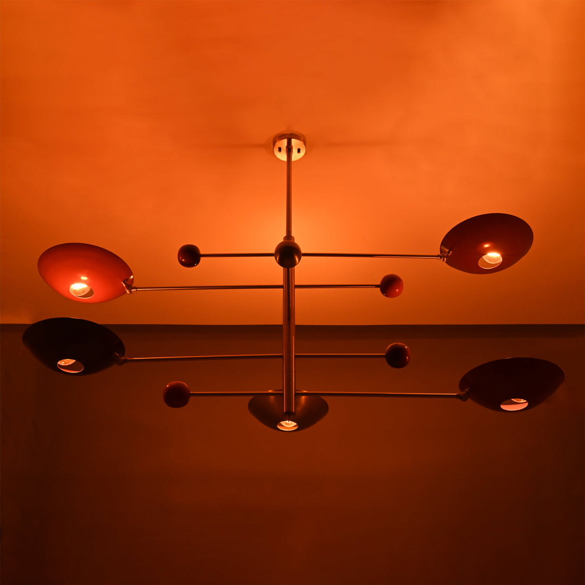 Brass mobile chandelier illuminated in warm ambient light, showcasing sculptural arms and red reflective bowl shades.