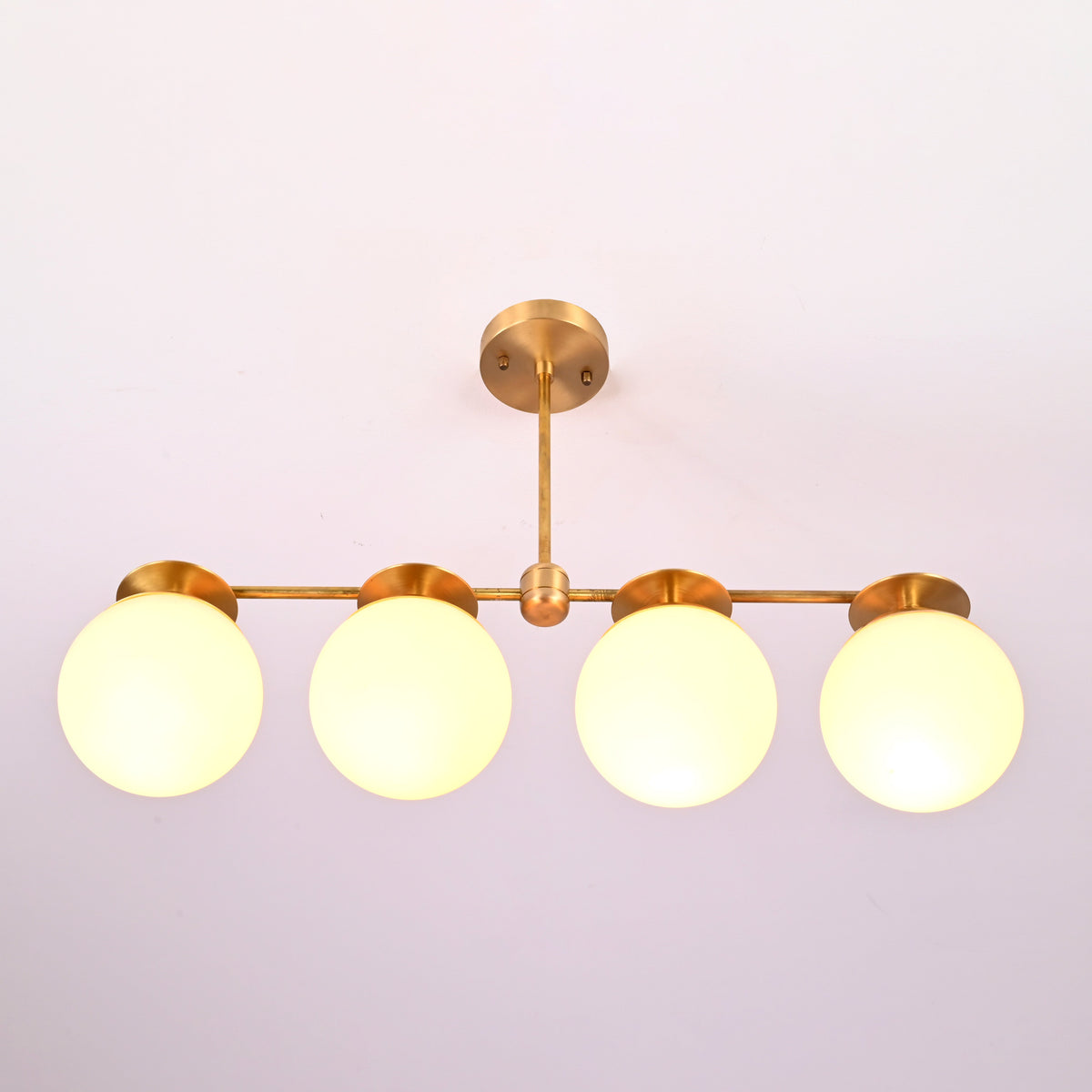 Close-up of opal glass globe shades on solid brass linear chandelier, highlighting warm diffused illumination.