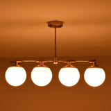 Front-facing view of brass linear chandelier with four opal glass globes in a low-light interior setting.