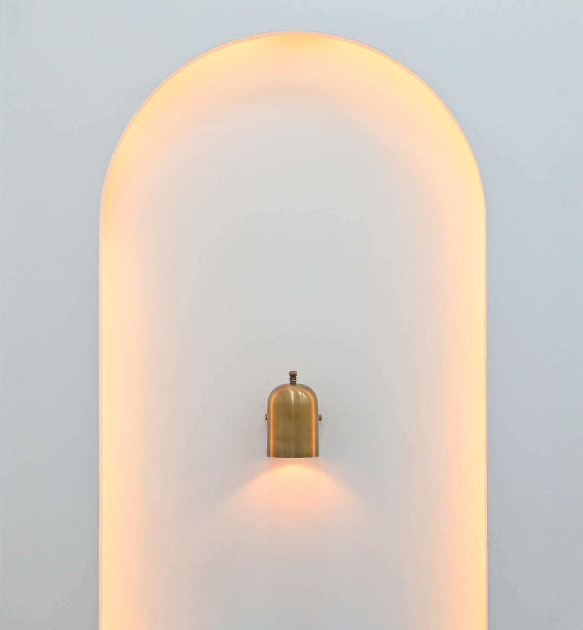 Cylindrical wall light in brass patina finish creating warm focused downward illumination on a light-colored wall