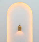 Cylindrical wall light in brass patina finish creating warm focused downward illumination on a light-colored wall