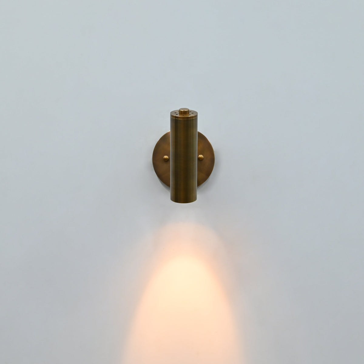 Side view of brass patina cylindrical wall sconce with adjustable-style support arm and round mounting plate