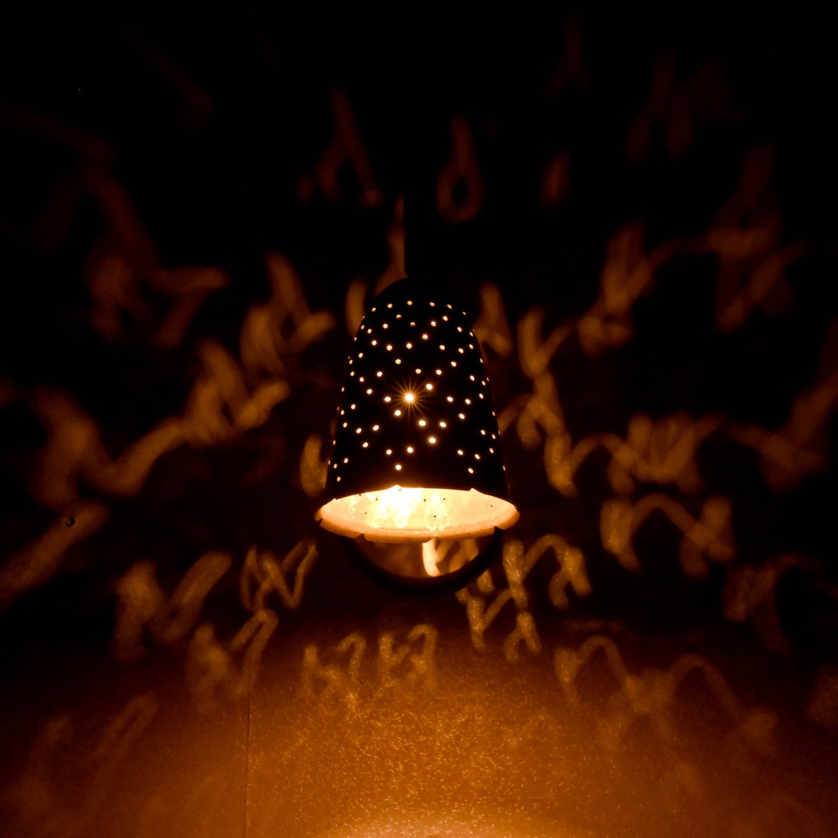 Brass perforated wall sconce glowing in dark room with decorative light shadows