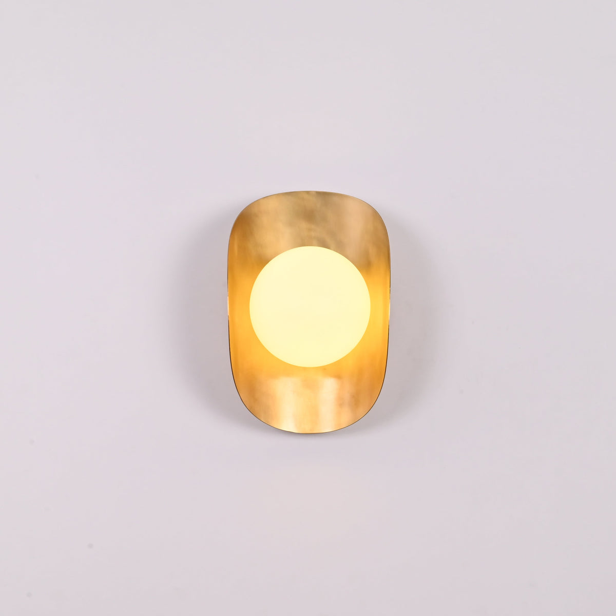 Brass shield globe sconce creating soft warm glow for luxury home and boutique interiors
