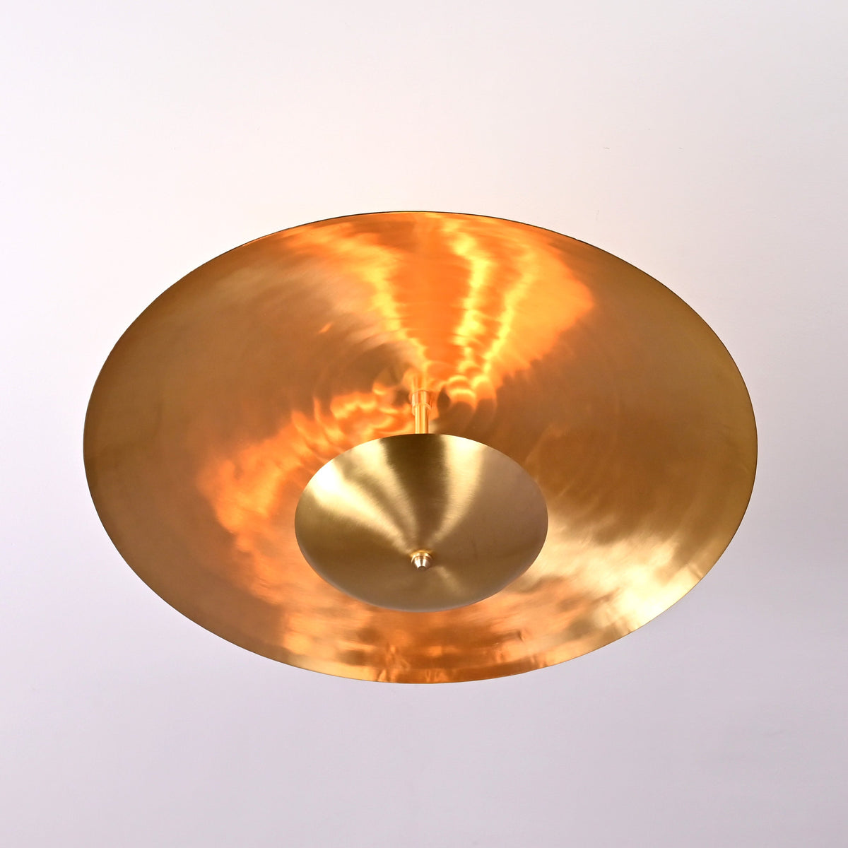 Bottom view of brass disc chandelier showing glowing indirect light and hammered brass reflection