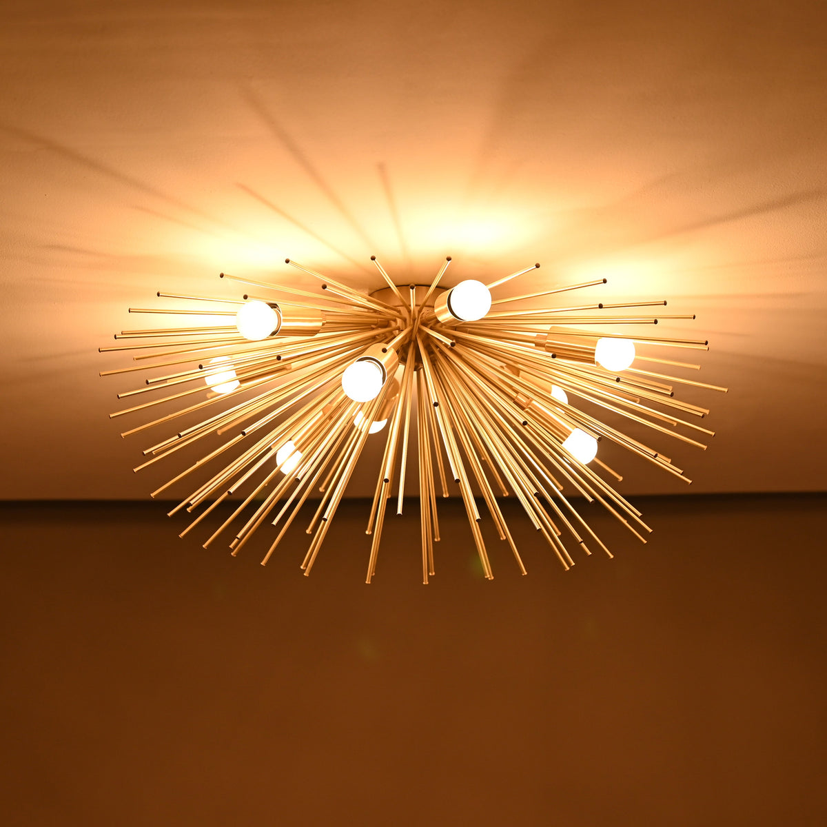 Brass urchin chandelier lit in a dark room, casting dramatic warm light patterns across the ceiling.