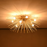 Brass urchin chandelier lit in a dark room, casting dramatic warm light patterns across the ceiling.