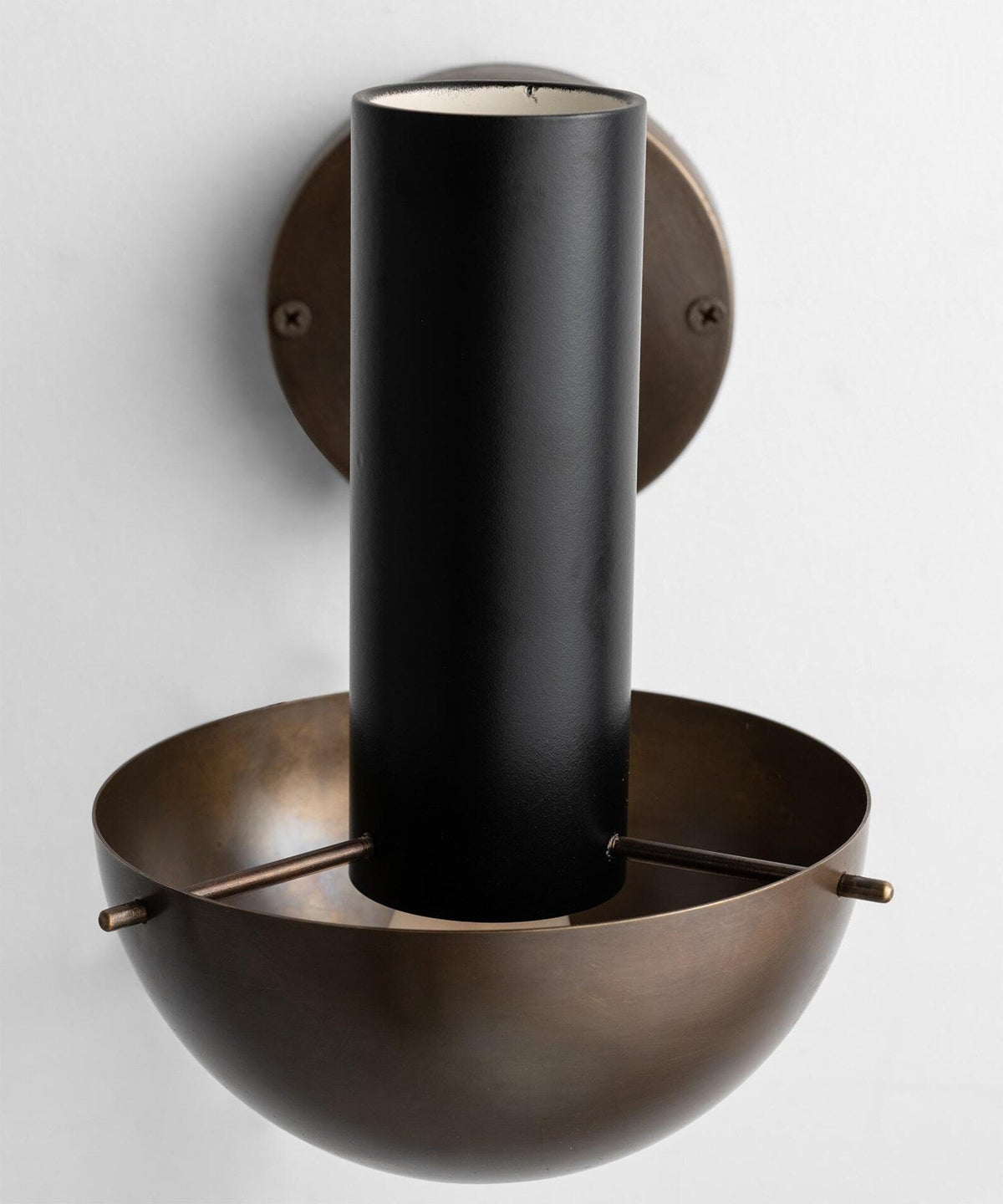 Close-up of brass wall lamp showing cylindrical upper form, solid brass wall mount, and hand-finished surface detailing.