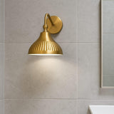 Modern brass dome wall sconce installed in bathroom setting with tiled wall and soft warm lighting.