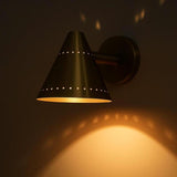 Brass cone wall sconce creating a decorative light pattern on the wall with warm, indirect illumination.
