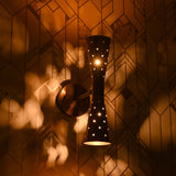 Close-up of brass double cone wall sconce lit, casting warm patterned light on wall