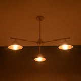 Warm-lit brushed brass chandelier with three cone shades, highlighting elegant sculpted industrial design.