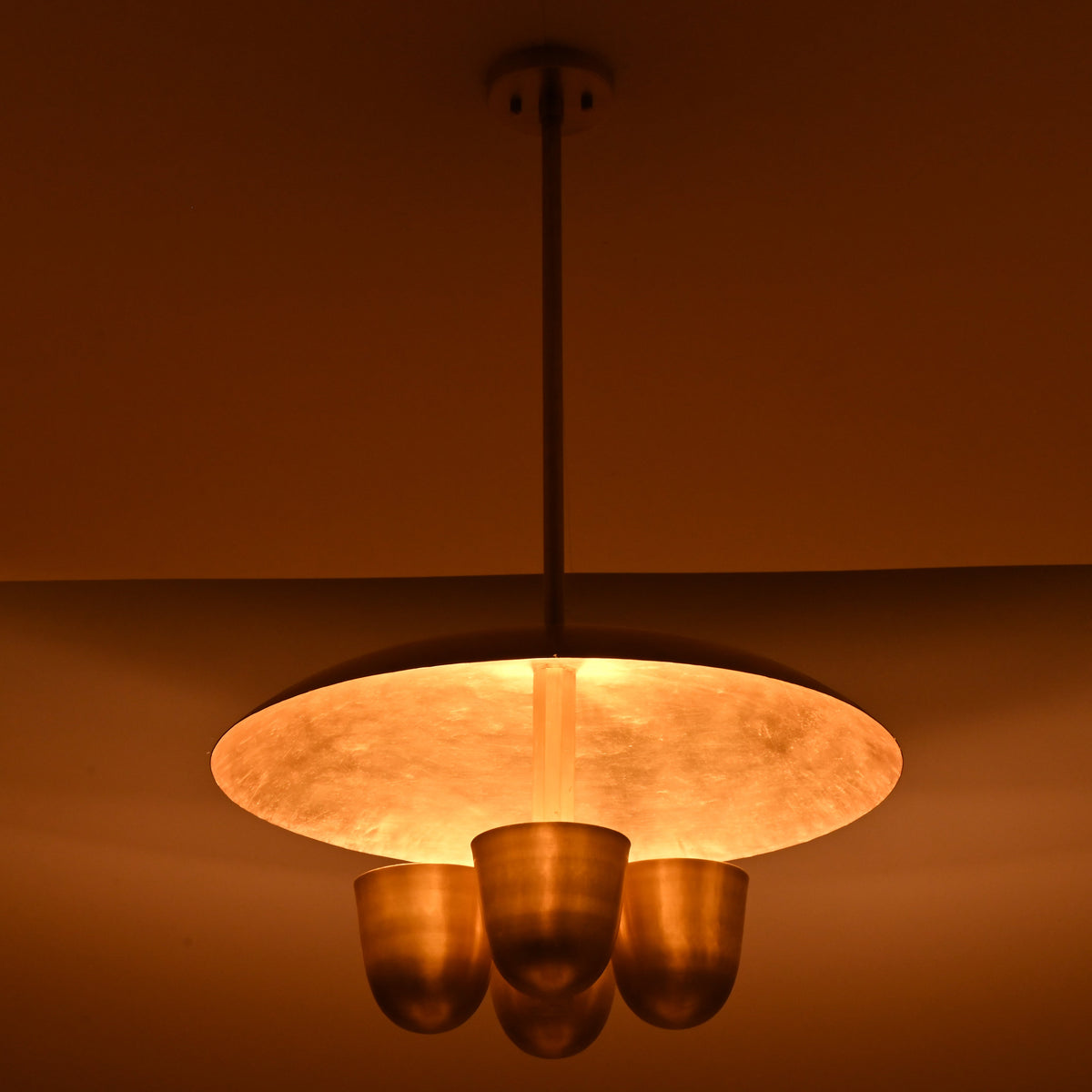 Side view of illuminated brushed brass disc chandelier with four bowl lights, soft warm glow highlighting brass textures
