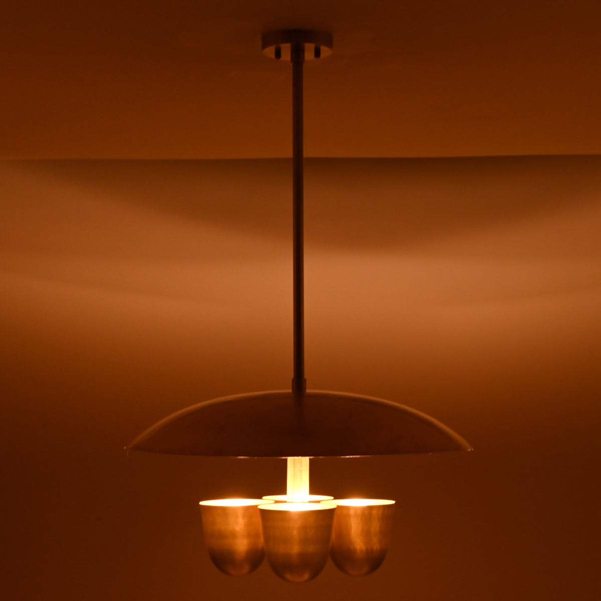 Brushed brass disc chandelier with four bowl shades illuminated, creating warm ambient indirect lighting in modern interiors