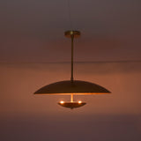 Brushed brass disc pendant illuminated in dark room creating soft indirect ambient lighting.