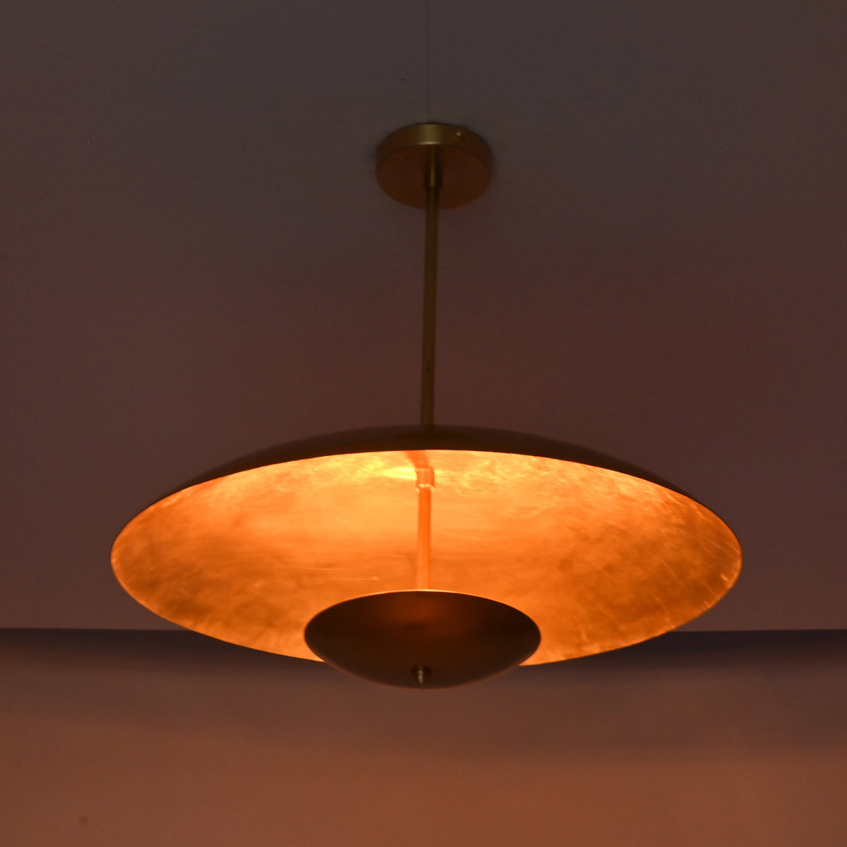 Underside view of brushed brass pendant showing warm reflected light and circular bowl form.