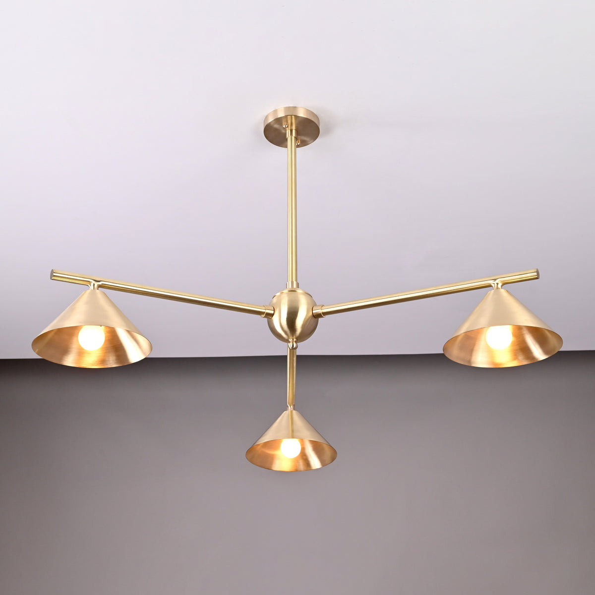 Three-arm brushed brass chandelier featuring sculpted cone shades and a minimalist industrial design.