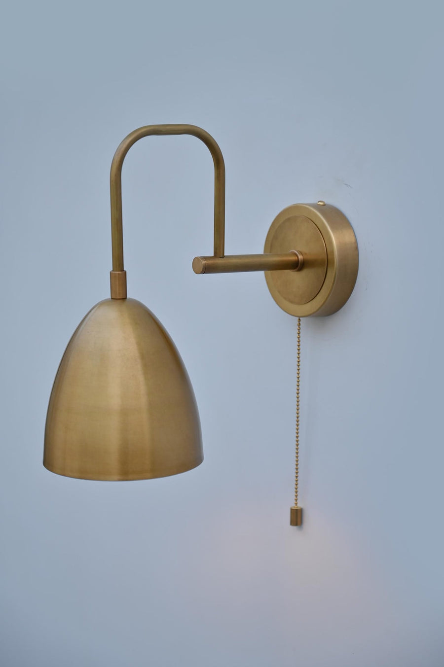 Side view of brass dome wall light with pull chain, handcrafted by Brass Leaf Studio in brushed brass finish for modern interiors.