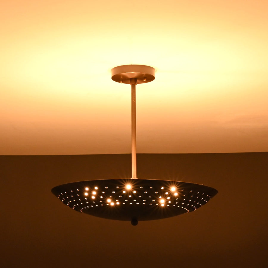 Brushed brass disc ceiling light illuminated with perforated design pattern