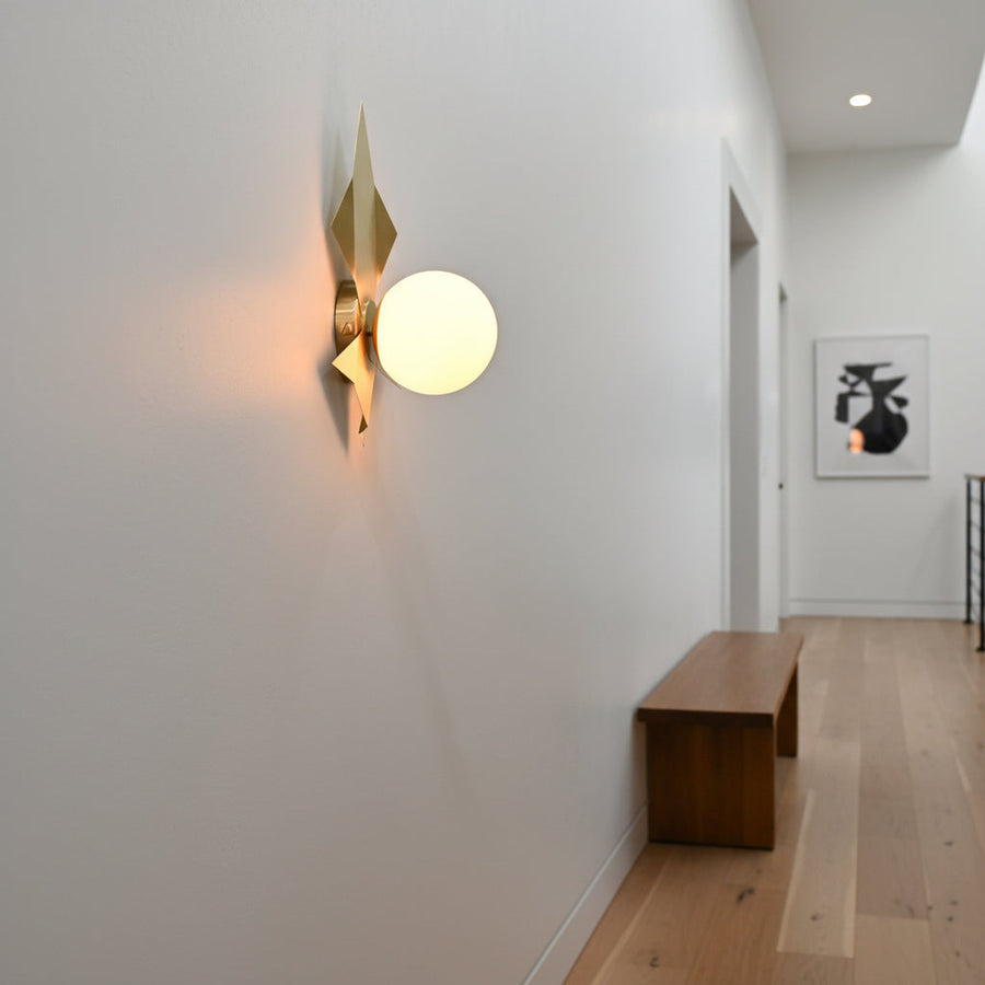 Raw brass leaf style wall sconce with glowing round glass globe creating warm decorative wall lighting