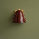 Burgundy cone wall sconce with brass detailing mounted on green accent wall