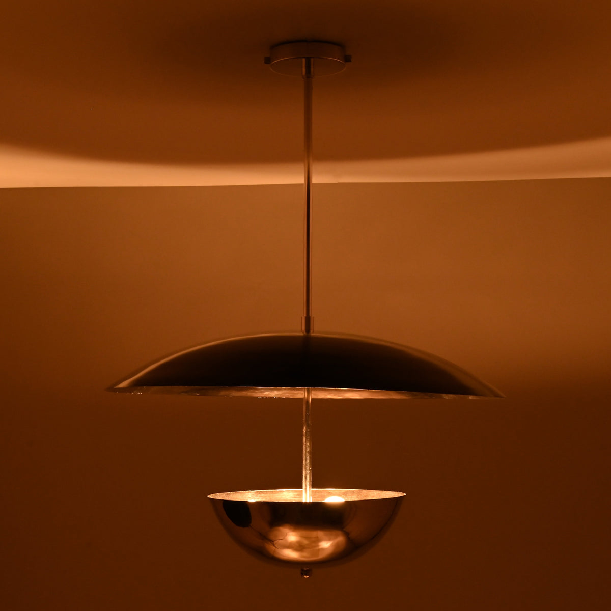 Chrome bowl-and-disc pendant light producing warm indirect illumination from below