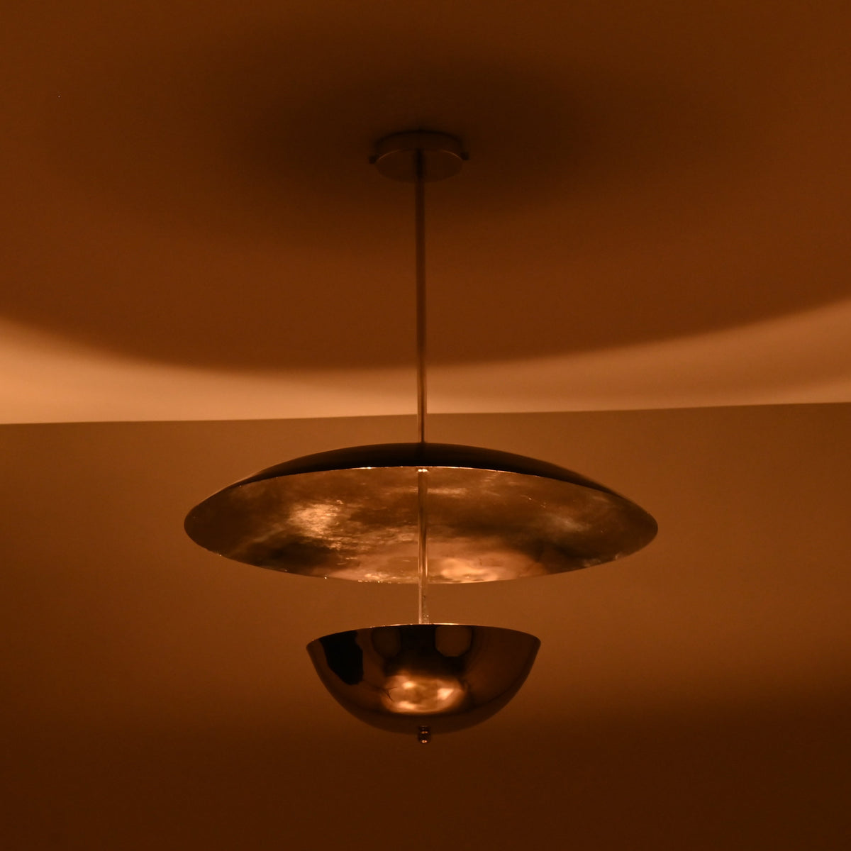 Chrome brass disc chandelier illuminated at night with warm ambient lighting and soft reflections