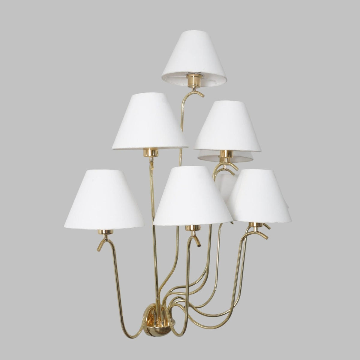 Side profile of handcrafted brass wall chandelier featuring layered white cone shades and graceful curved arms.