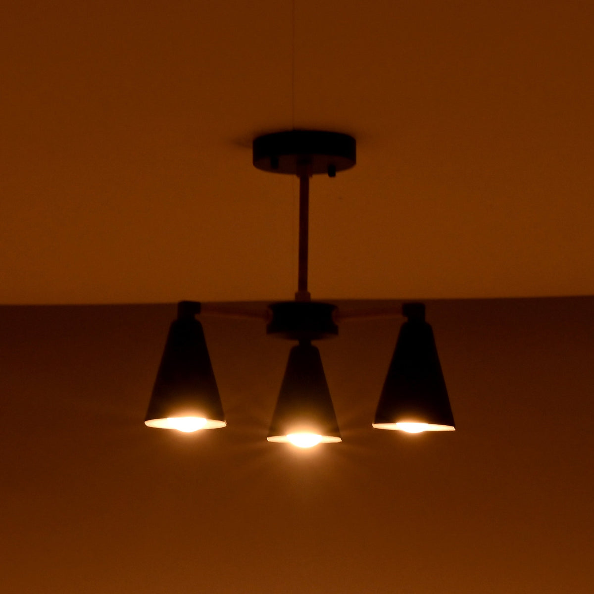 Three light cone brass chandelier creating warm ambient lighting in a dark interior setting