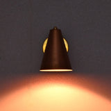 Brass and copper wall sconce lit in a dark setting, casting a warm ambient glow on the wall.