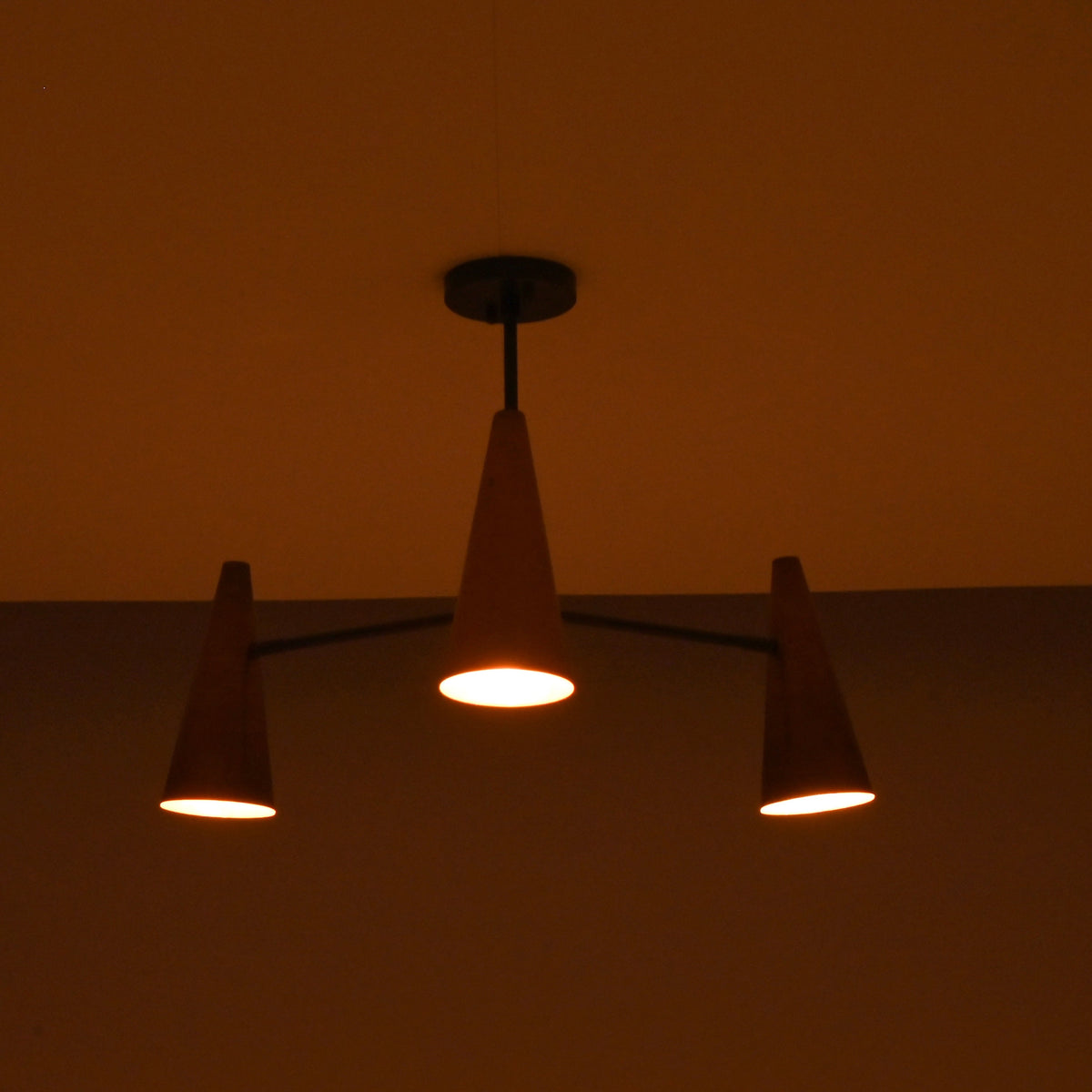Three light copper cone chandelier in dark setting creating moody, atmospheric ceiling lighting