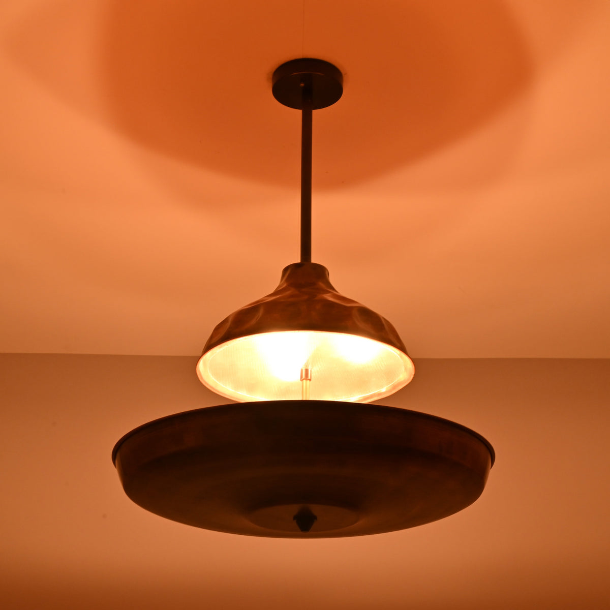Copper disc chandelier casting warm ambient indirect lighting, creating a soft glow across the ceiling