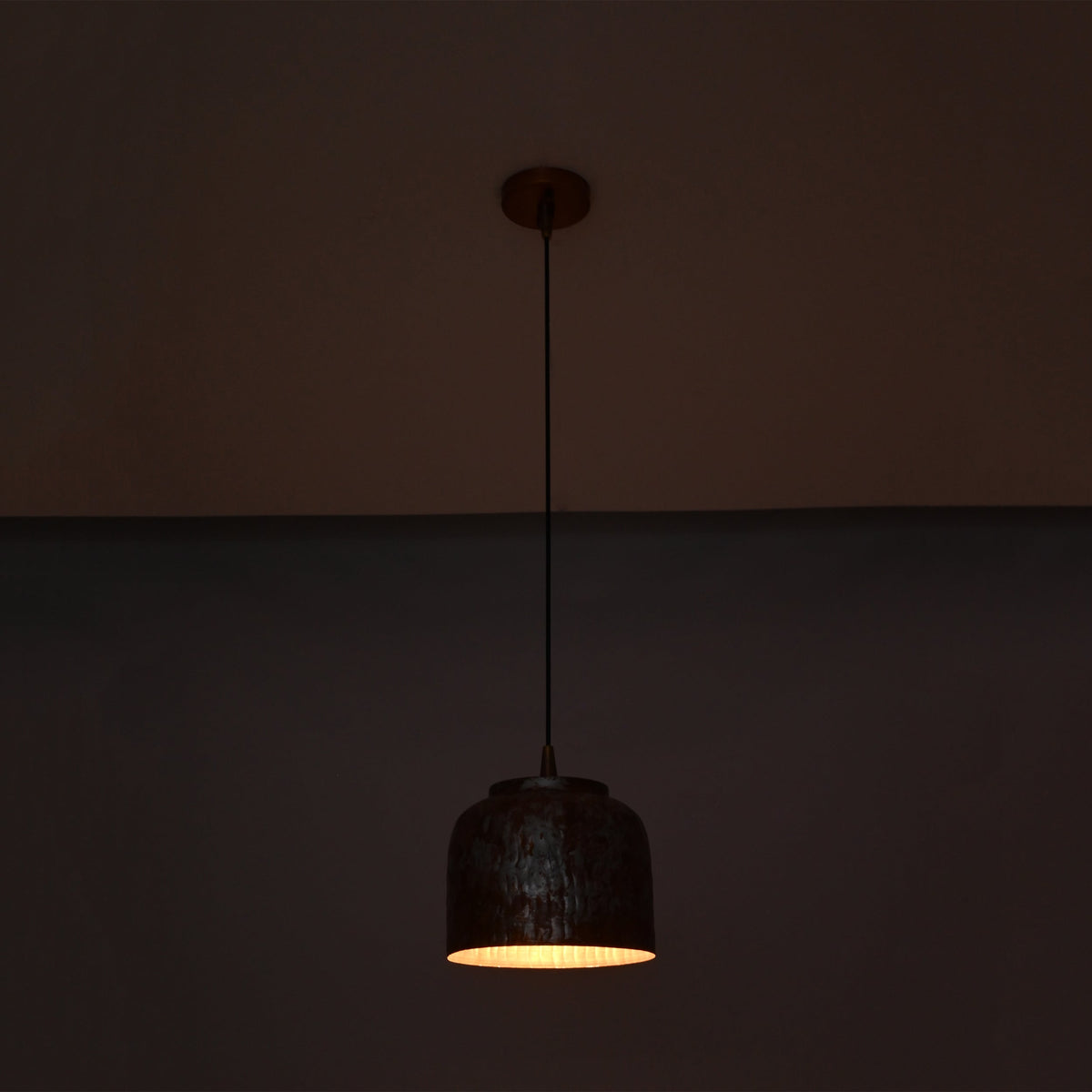 Cora pendant light glowing warmly from below, highlighting the compact drum shade and textured copper finish