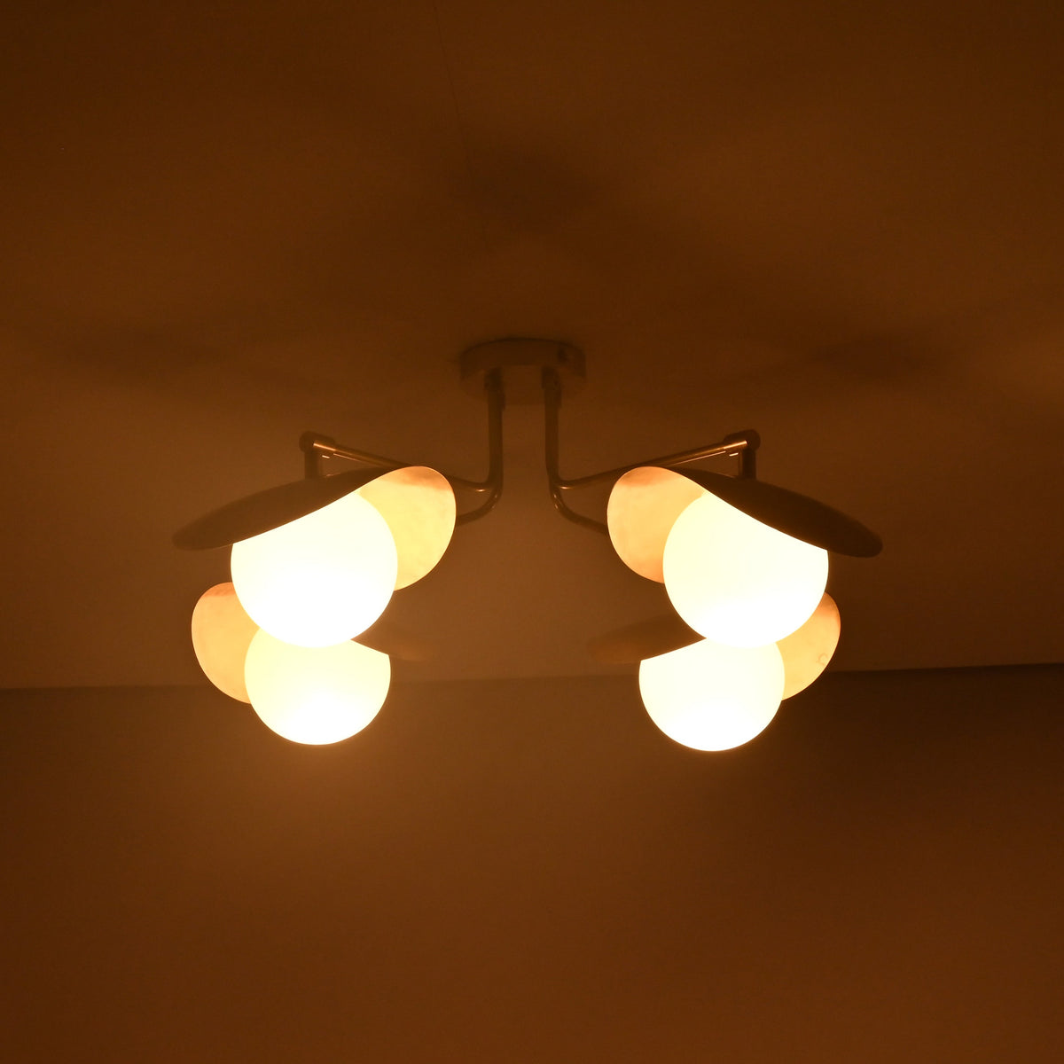 Artistic ceiling view of Curva designer brass flush mount highlighting curved brass shades, globe lights, and soft indirect illumination.