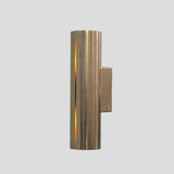 Handmade cylindrical brass wall sconce with vertical glowing slit design, crafted by Brass Leaf Studio for modern and industrial interiors.