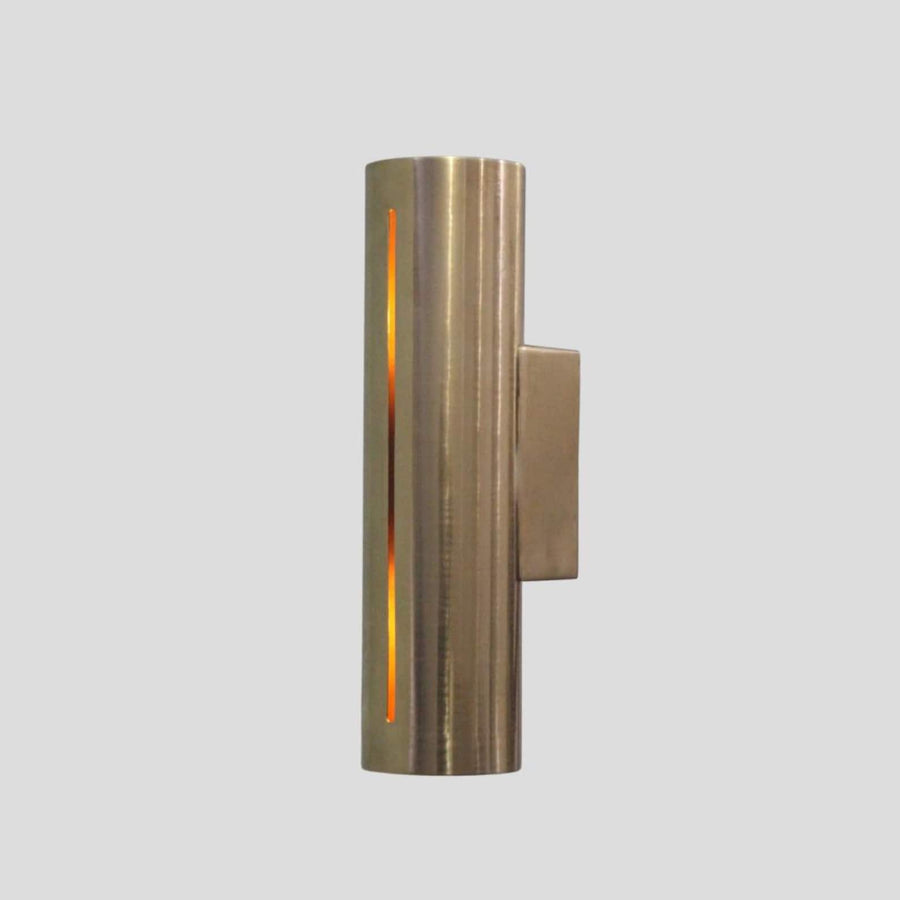 Handmade cylindrical brass wall sconce with vertical glowing slit design, crafted by Brass Leaf Studio for modern and industrial interiors.