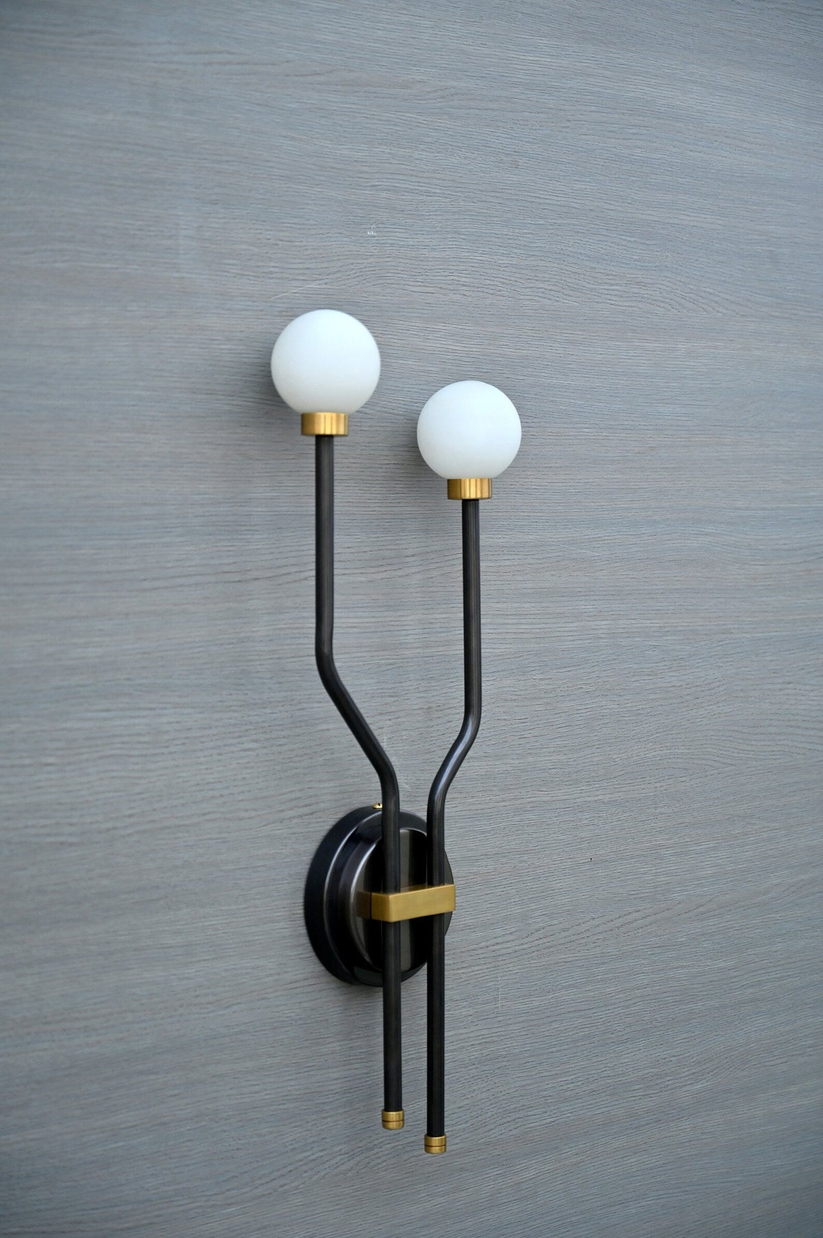 Angled close-up of handcrafted double globe wall sconce with brass accents and frosted globes