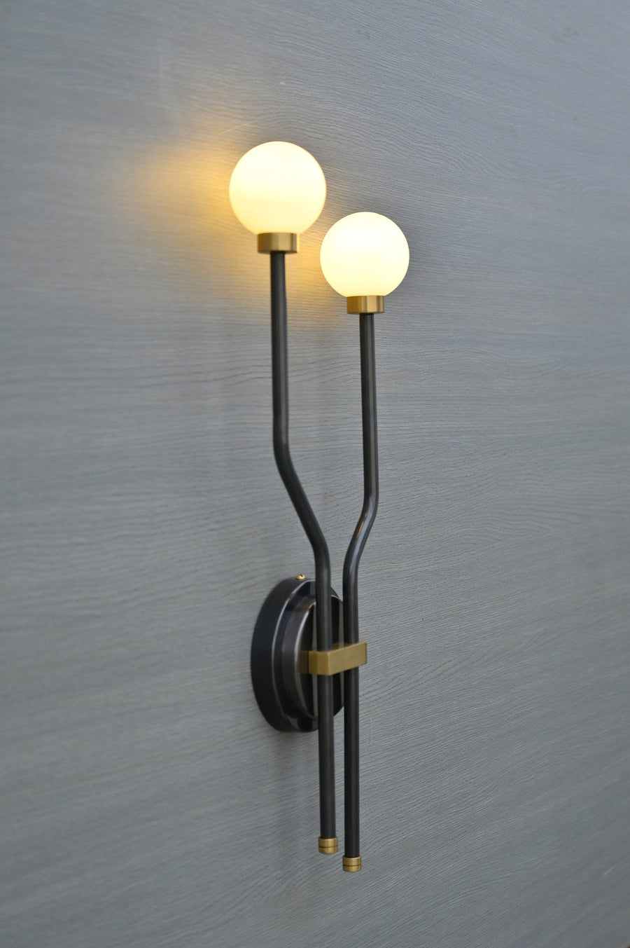 Front view of double globe brass wall sconce with minimalist black frame and frosted globes