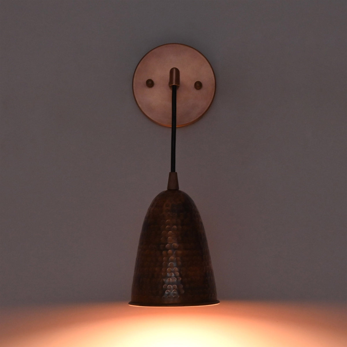 Front view of the Hudson Modern Hammered Copper Cone Wall Sconce mounted on a wall with warm downward illumination, showcasing the handcrafted hammered copper cone shade and minimalist design.