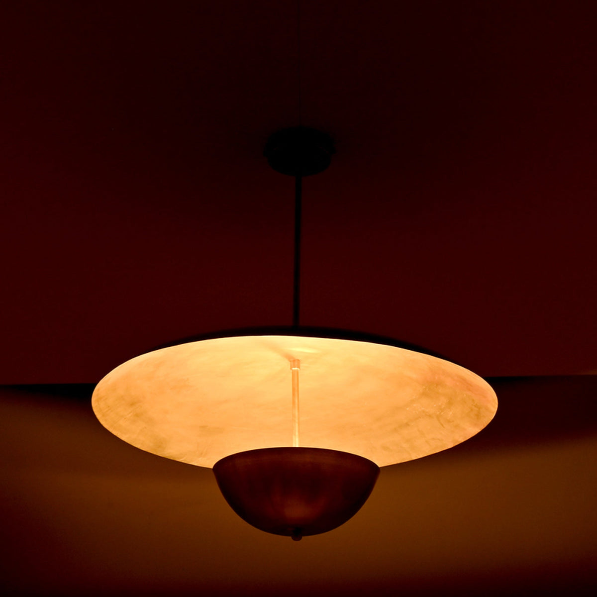 Close-up night view of brass dual-shade pendant highlighting the warm inner glow and reflective brass surfaces.