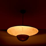 Close-up night view of brass dual-shade pendant highlighting the warm inner glow and reflective brass surfaces.