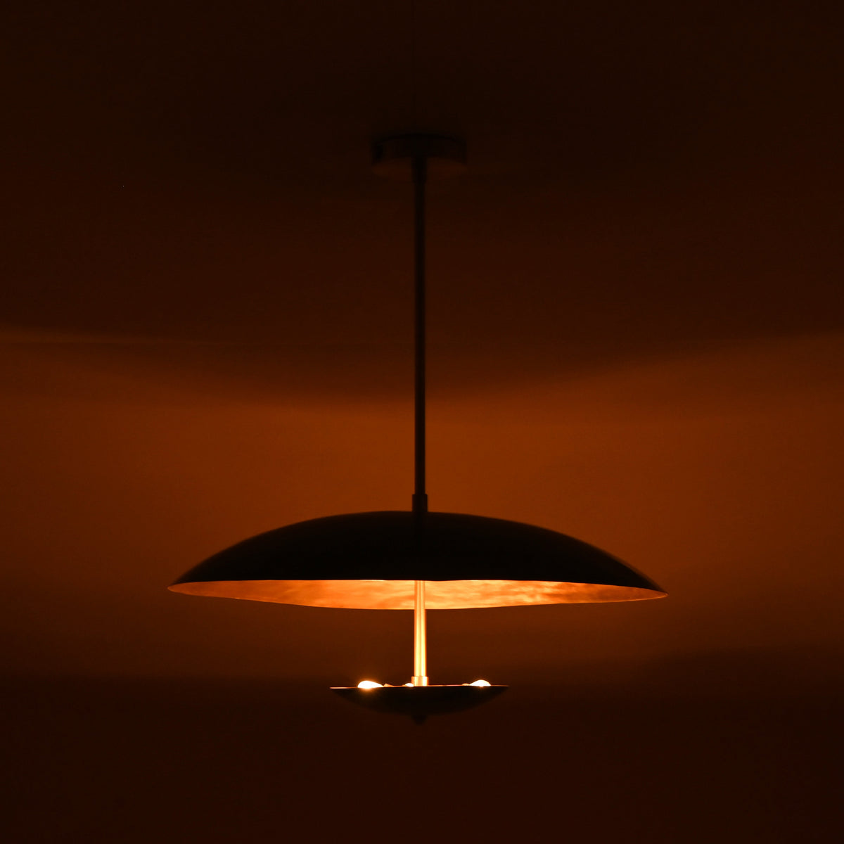 Handcrafted emerald green brass pendant light at night illuminating space with rich warm brass glow