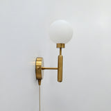 Raw brass pull-chain globe wall sconce with round frosted globe, vertical stem, and side-view mounting plate.