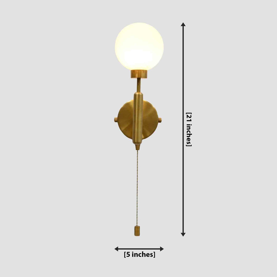 Raw brass pull-chain globe wall sconce with round frosted globe, vertical stem, and side-view mounting plate.