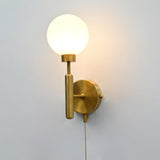 Illuminated raw brass wall sconce with round frosted globe, vertical stem, circular backplate, and pull chain.