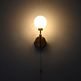 Illuminated raw brass wall sconce with round frosted globe, vertical stem, circular backplate, and pull chain.